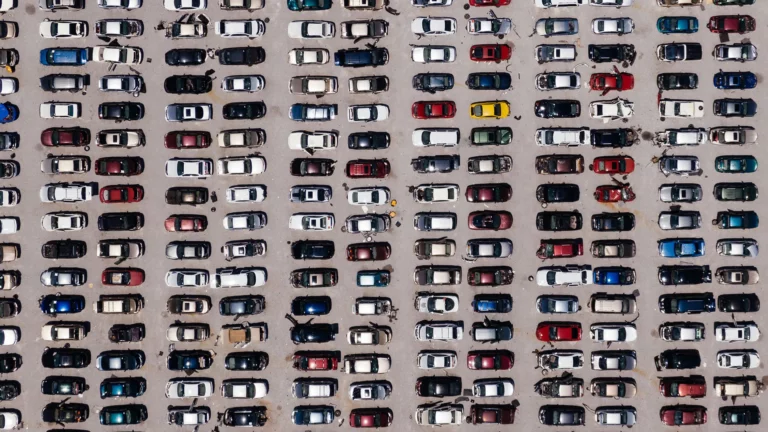 Vista aerea di un parcheggio con molte auto parcheggiate in file ordinate, alcune danneggiate e altre in buone condizioni